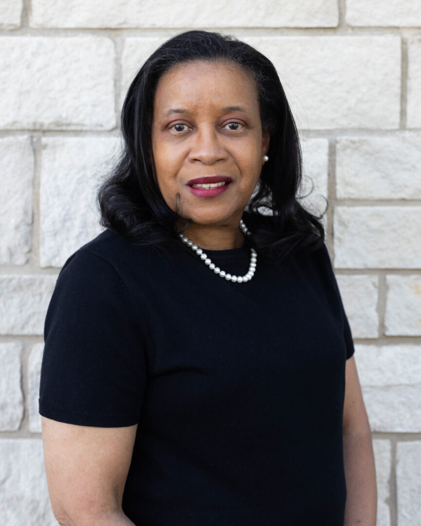 A woman in black shirt standing next to a brick wall.