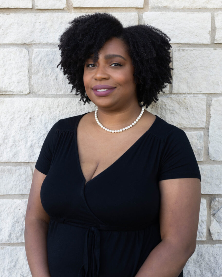 A woman standing in front of a brick wall.