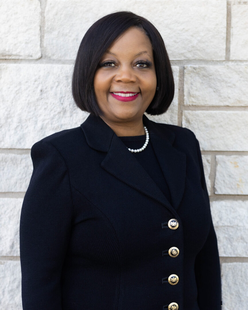 A woman in black jacket standing next to a brick wall.