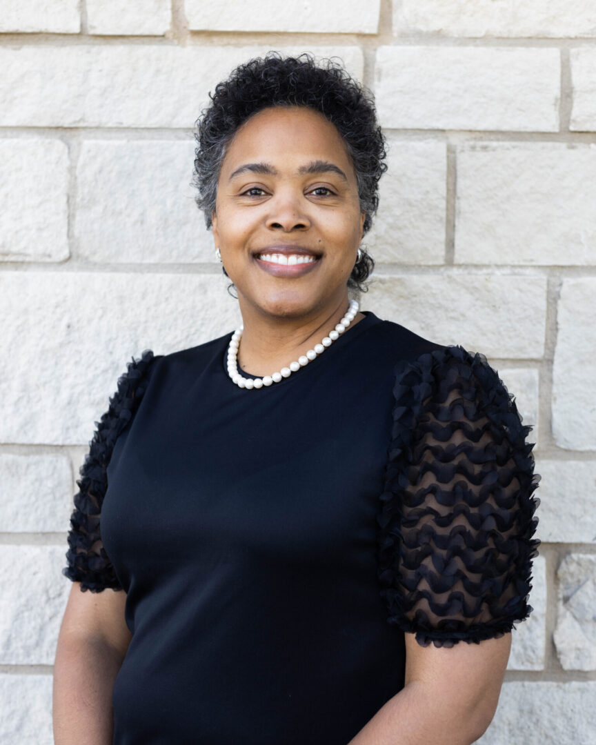 A woman in black shirt standing next to a brick wall.