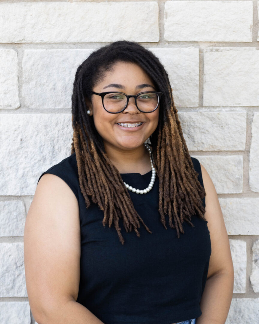 A woman with dreads standing in front of a brick wall.