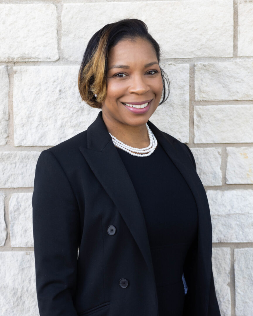 A woman in black jacket standing next to a brick wall.