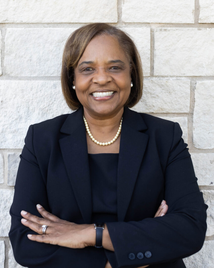 A woman in black jacket standing next to a brick wall.