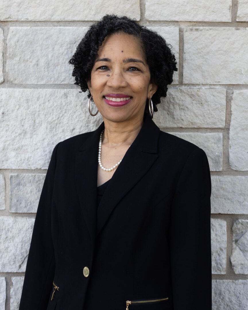 A woman in black jacket standing next to a brick wall.