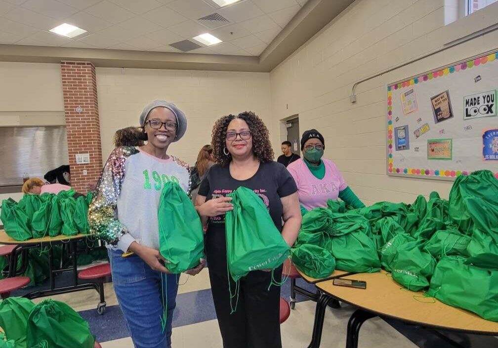 Two women holding green bags in a room.